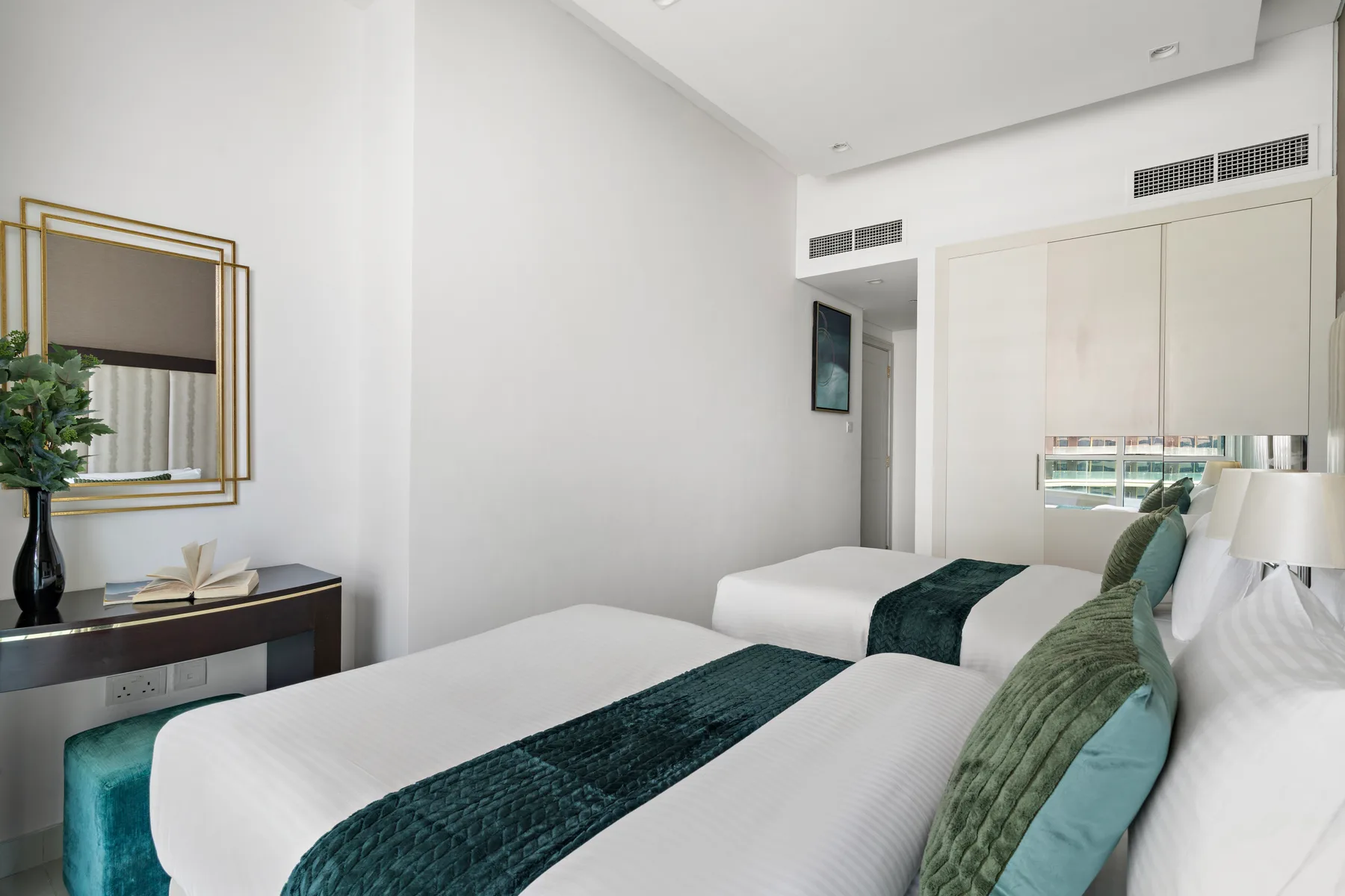 Un dormitorio luminoso con ropa de cama blanca y caminos verde oscuro.