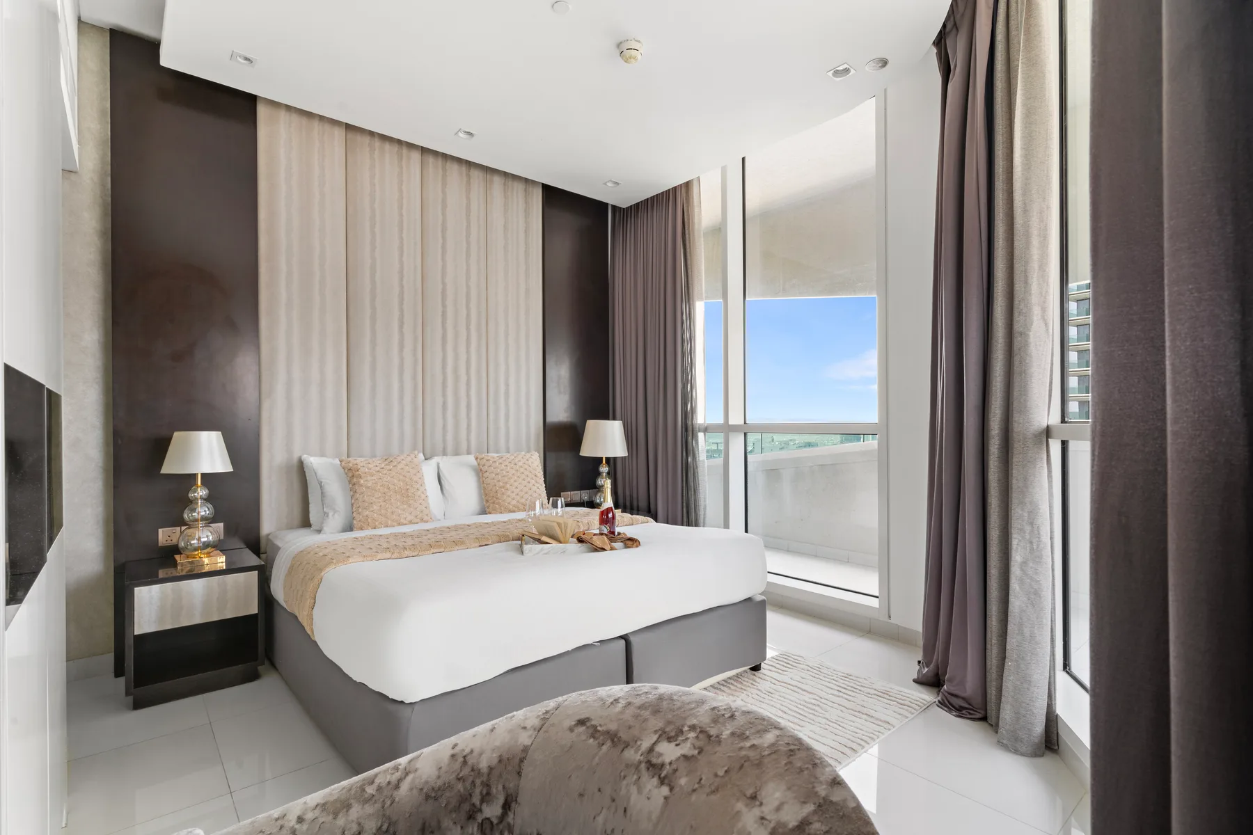 Un dormitorio luminoso con una cama tendida junto a ventanas de piso a techo.