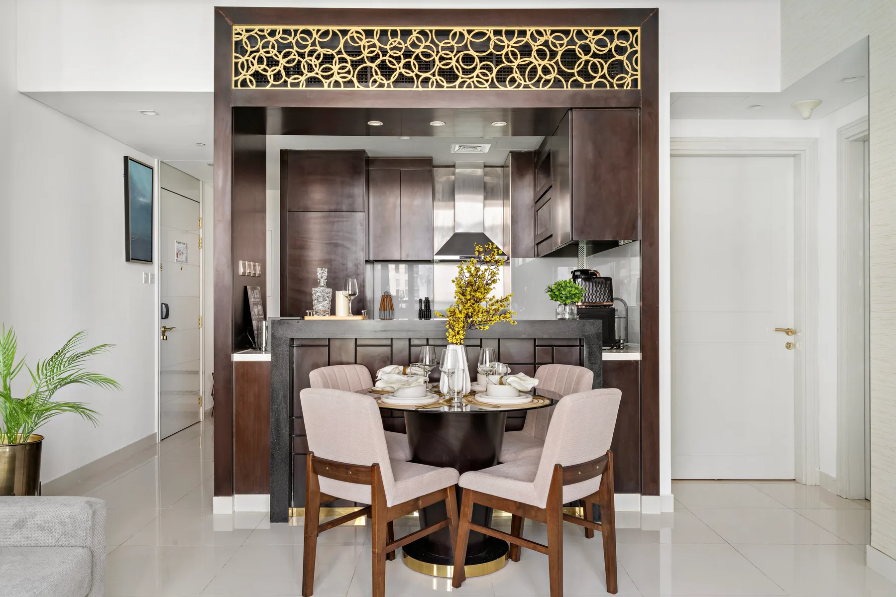 Una mesa de comedor con sillas está frente a una cocina compacta con gabinetes oscuros.