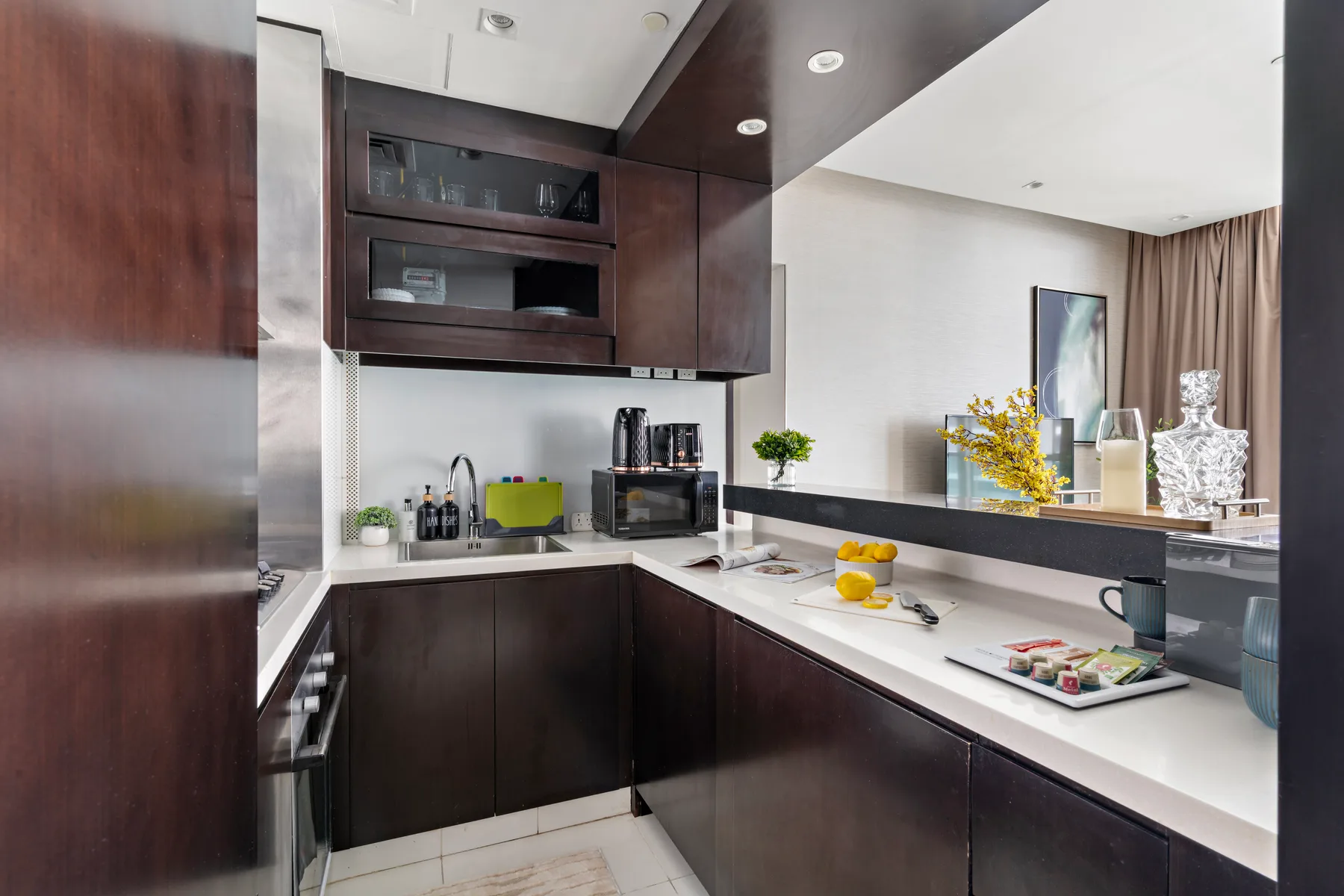 Una cocina moderna con gabinetes oscuros, encimeras blancas y un pequeño comedor.