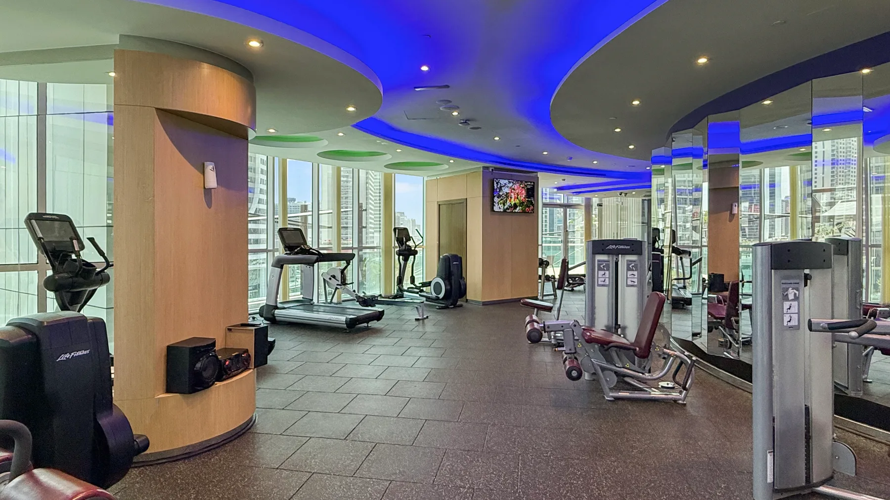 Un gimnasio moderno con máquinas de ejercicio, pesas y luces azules en el techo.