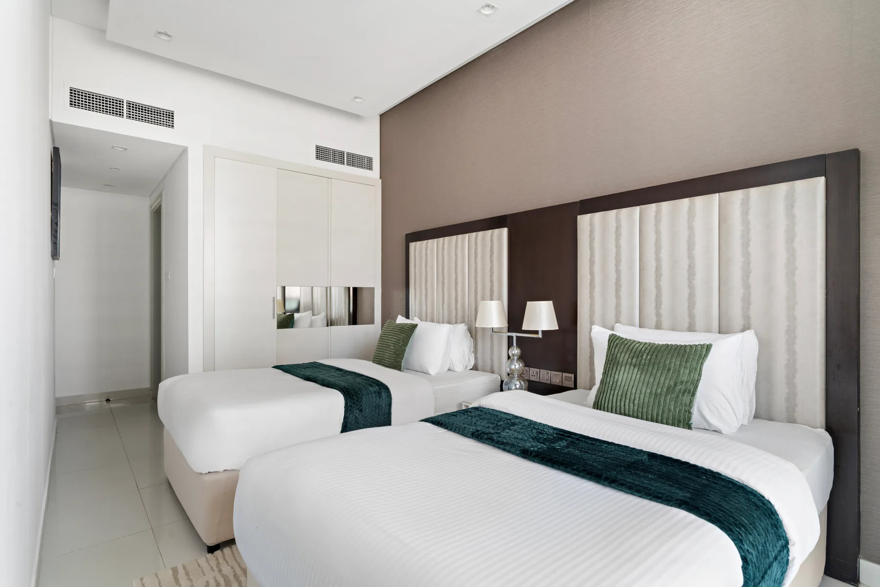 Un dormitorio con dos camas, ropa de cama blanca y cojines verdes.