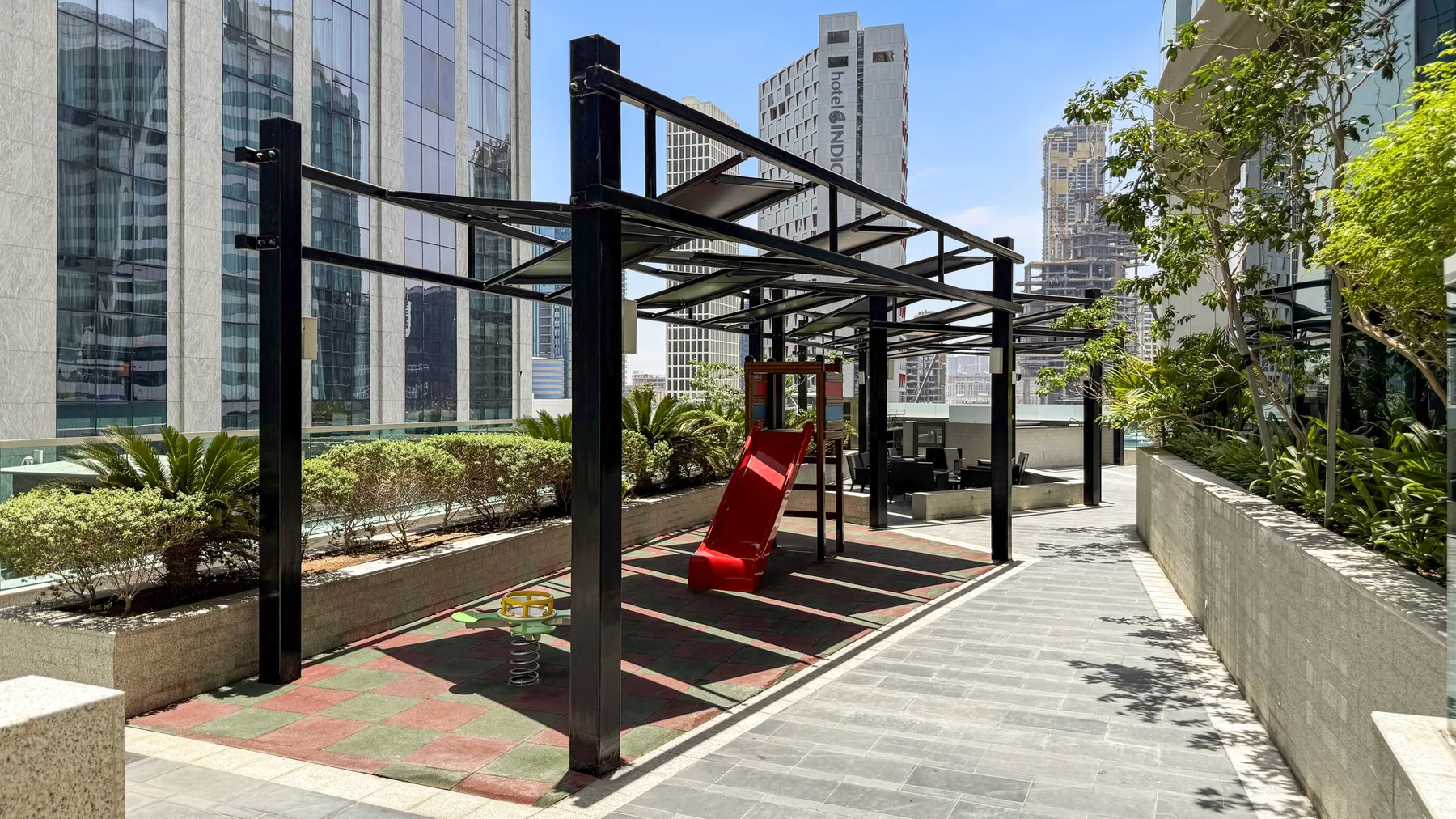 Un patio exterior tiene una estructura de juego metálica negra junto a un camino pavimentado.