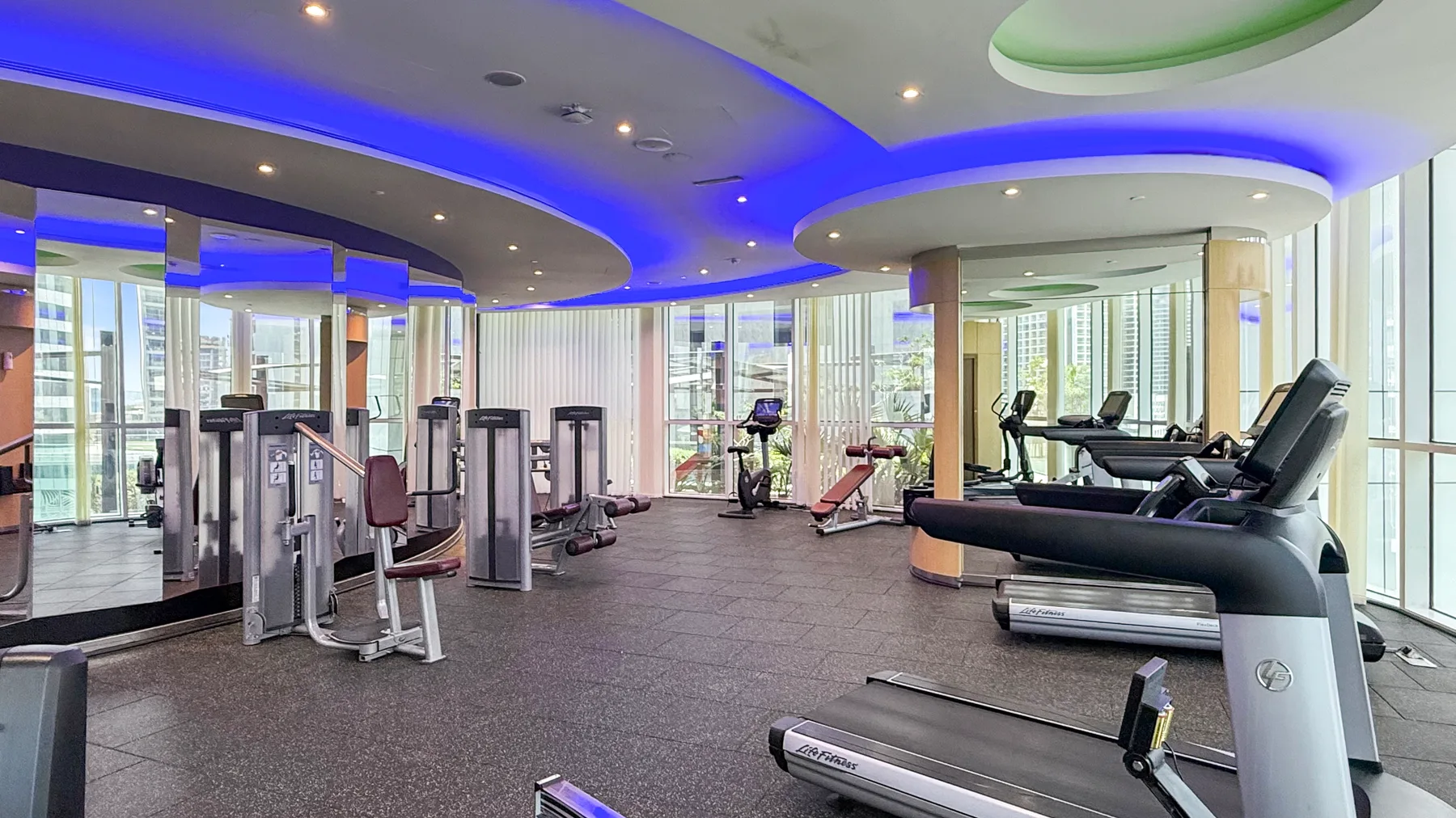Un gimnasio con máquinas de ejercicio y cintas de correr bajo luces azules en el techo.