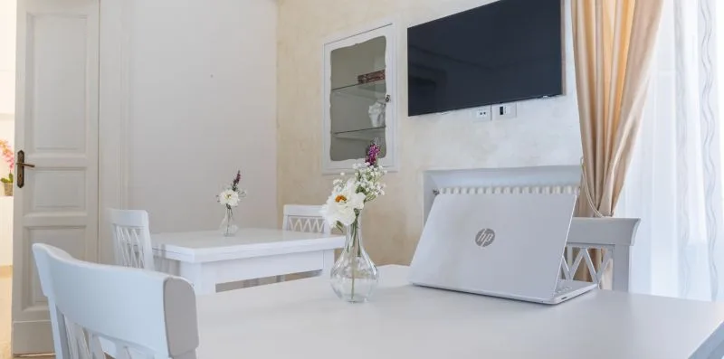 A bright room with white tables, flowers, and a wall-mounted television.
