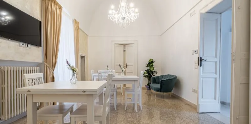 Un comedor luminoso con una mesa blanca, sillas y un sillón verde.