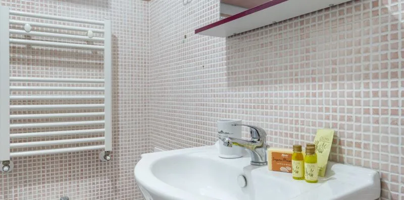 A bathroom sink with a faucet and toiletries beneath a tiled wall.