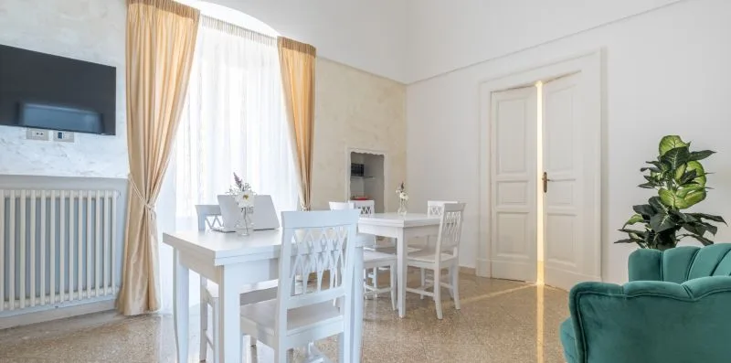 Un comedor luminoso con una mesa blanca, sillas y ventanas altas con cortinas.
