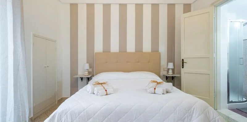A bedroom with a bed against a striped wall and a doorway to the bathroom.