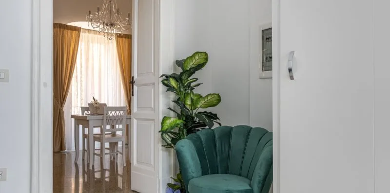 Un comedor luminoso con mesa y sillas se ve detrás de un sillón verde azulado.