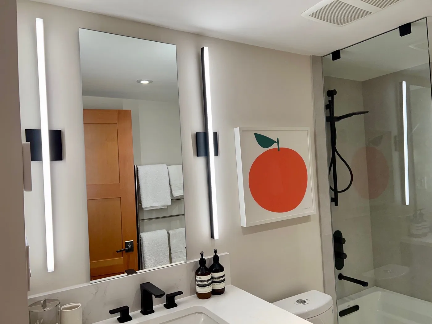 Un baño moderno con una ducha de vidrio y un espejo grande en la pared.
