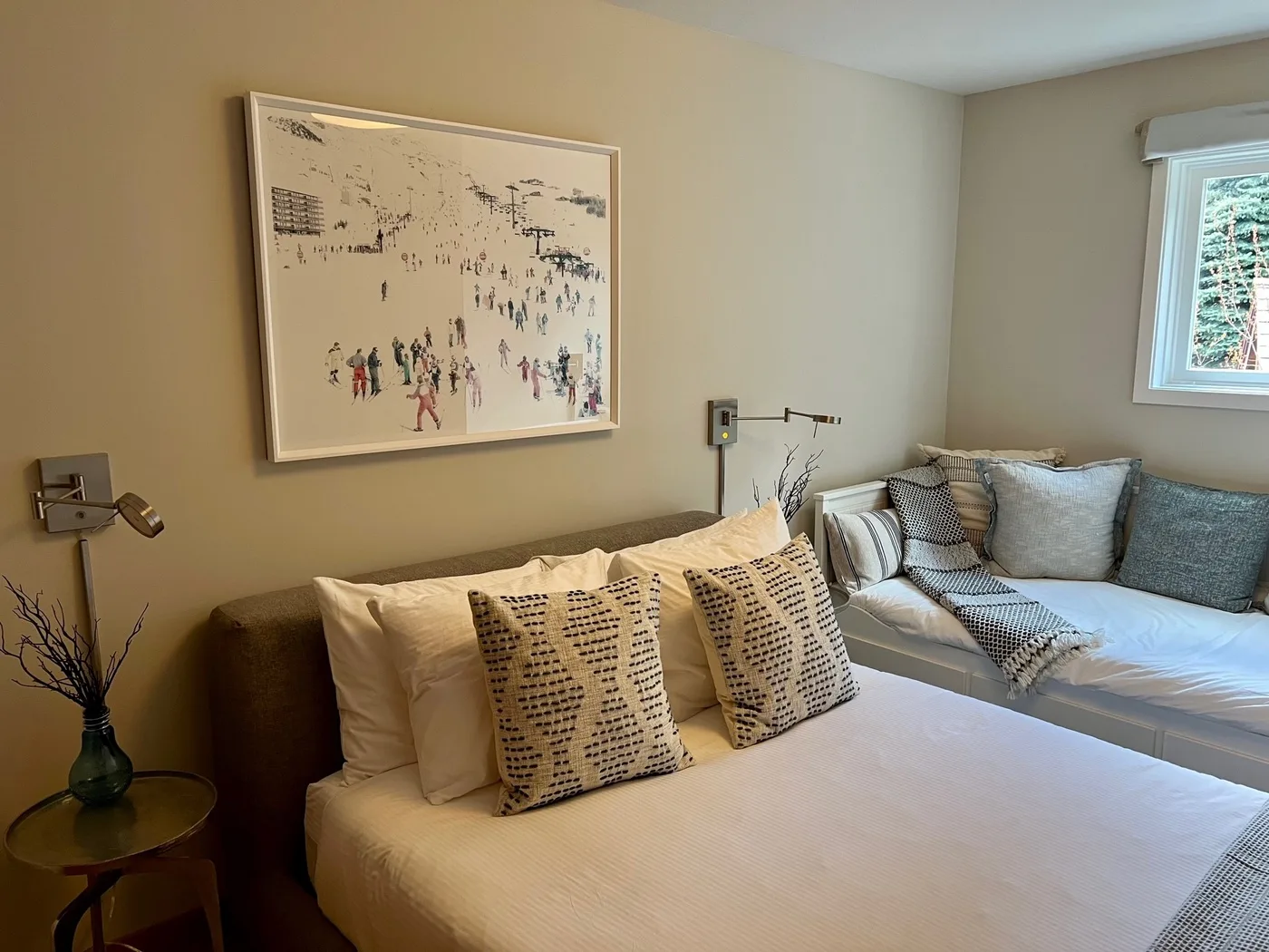Un dormitorio con dos camas, ropa de cama neutra y una lámina enmarcada en la pared.