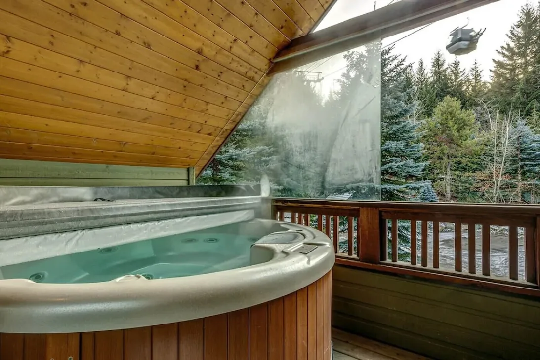 Una bañera de hidromasaje está junto a una ventana amplia con vistas a un paisaje boscoso.