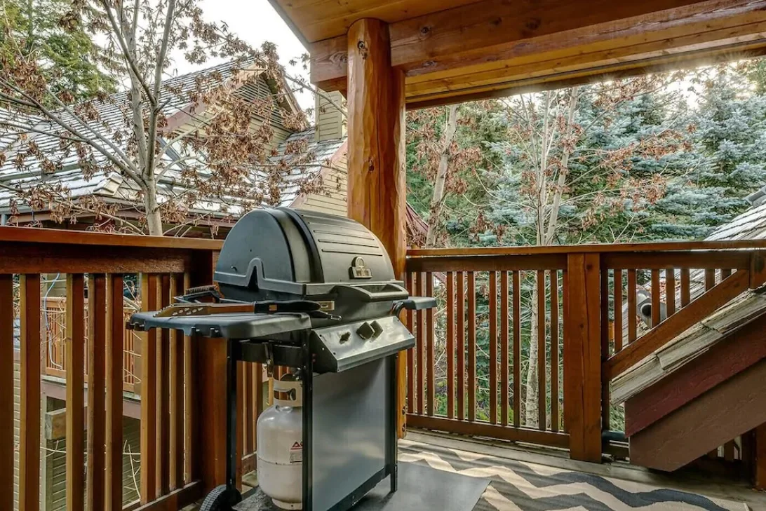 Una terraza cubierta de madera con una parrilla de gas y árboles al otro lado de la barandilla.
