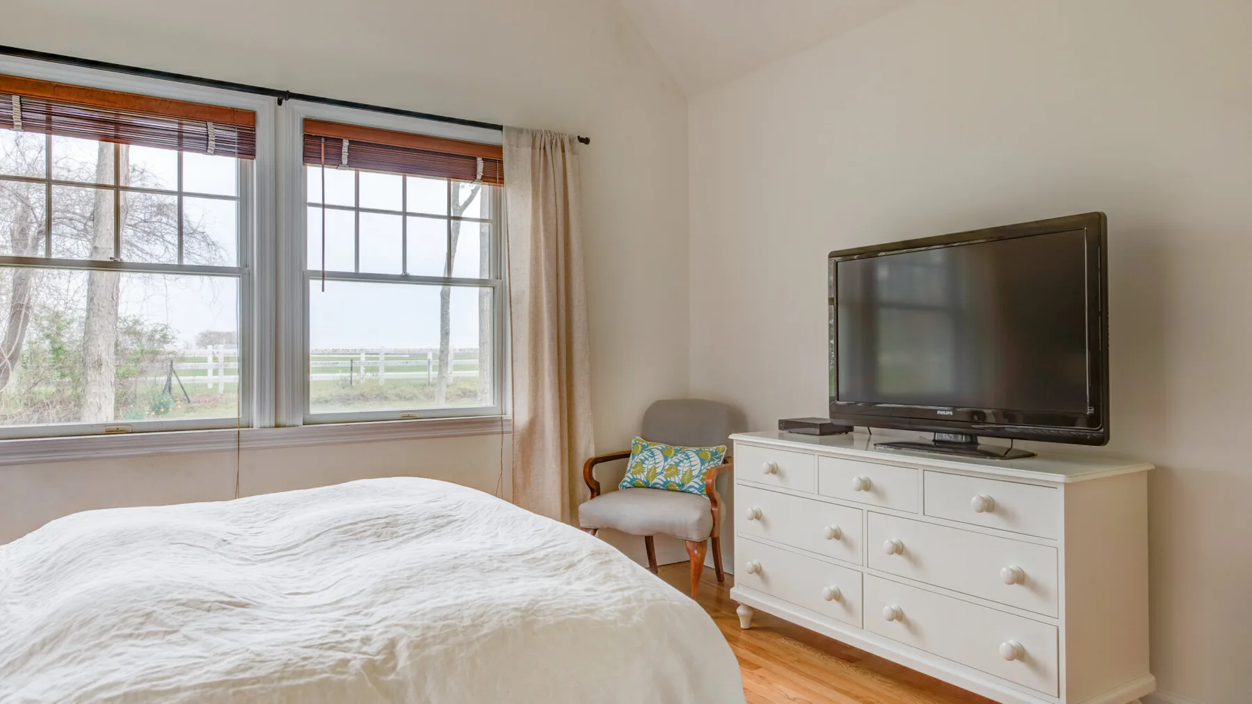 Un dormitorio luminoso con una cama junto a grandes ventanas y un televisor.