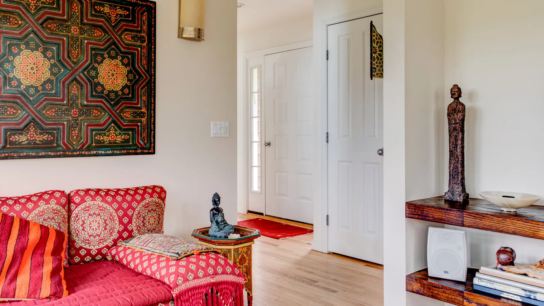 Una sala colorida con asientos estampados, un tapiz enmarcado y un mueble de madera.