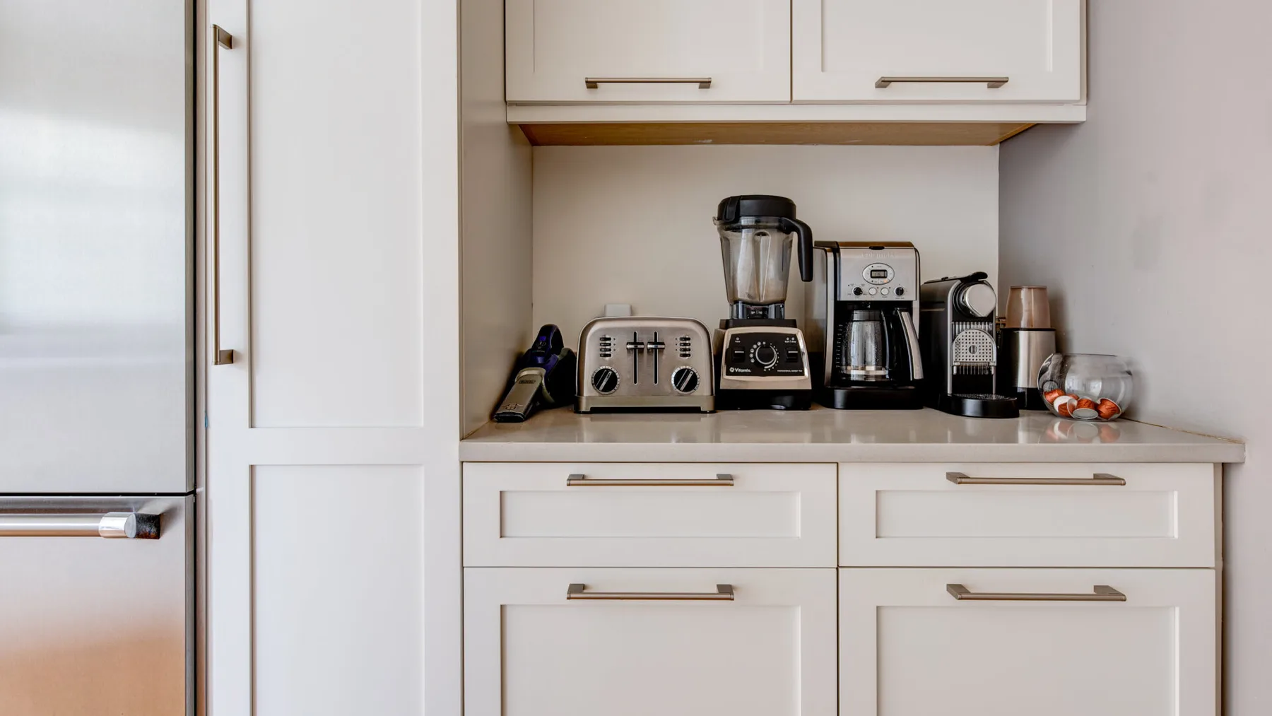 Una encimera de cocina con pequeños electrodomésticos está bajo armarios blancos.
