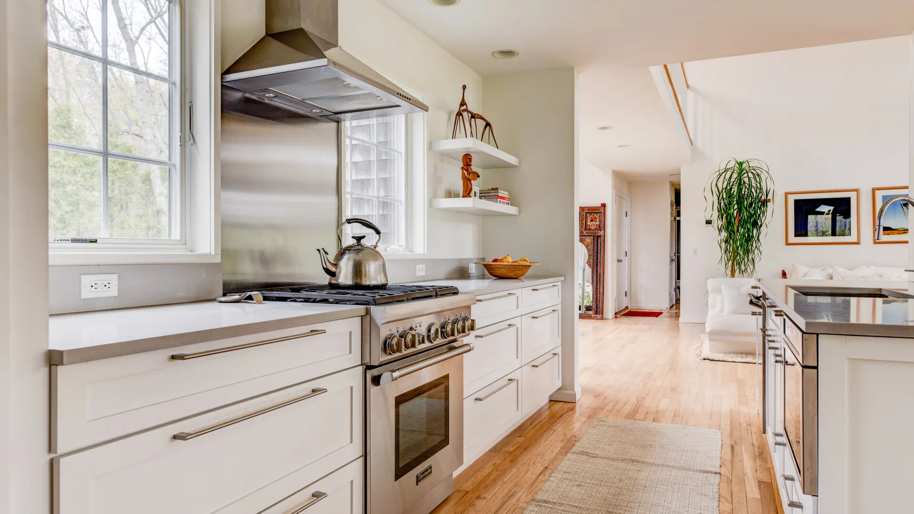Una cocina luminosa con gabinetes blancos, una estufa y un pasillo central largo.