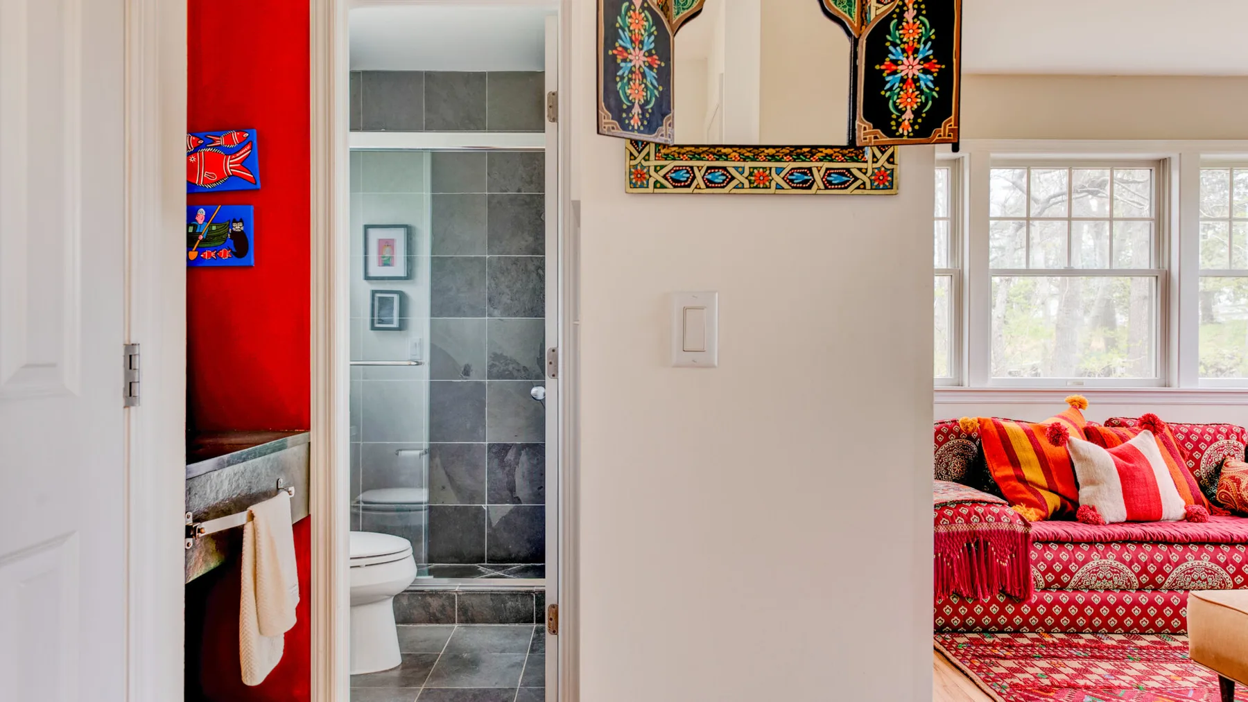 Un baño junto a una zona de estar con un sofá rojo de estampado llamativo.