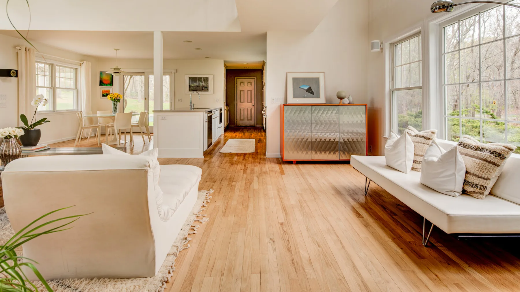 Una sala luminosa con asientos junto a grandes ventanas y un comedor abierto.
