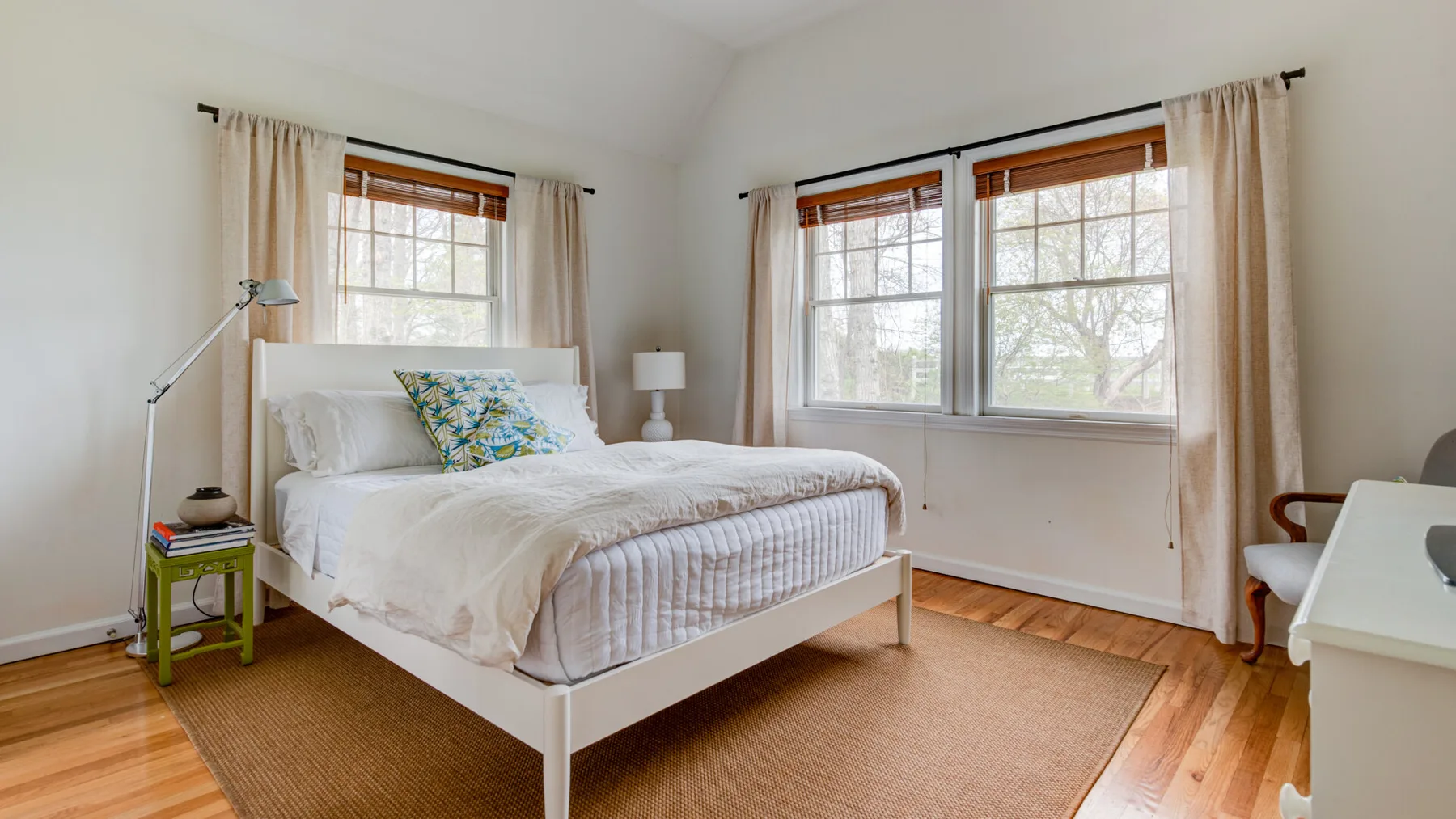 Un dormitorio luminoso con una cama, ventanas grandes y una alfombra tejida.