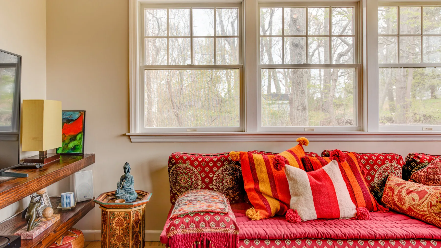 Una sala de estar con un sofá rojo estampado bajo grandes ventanas.