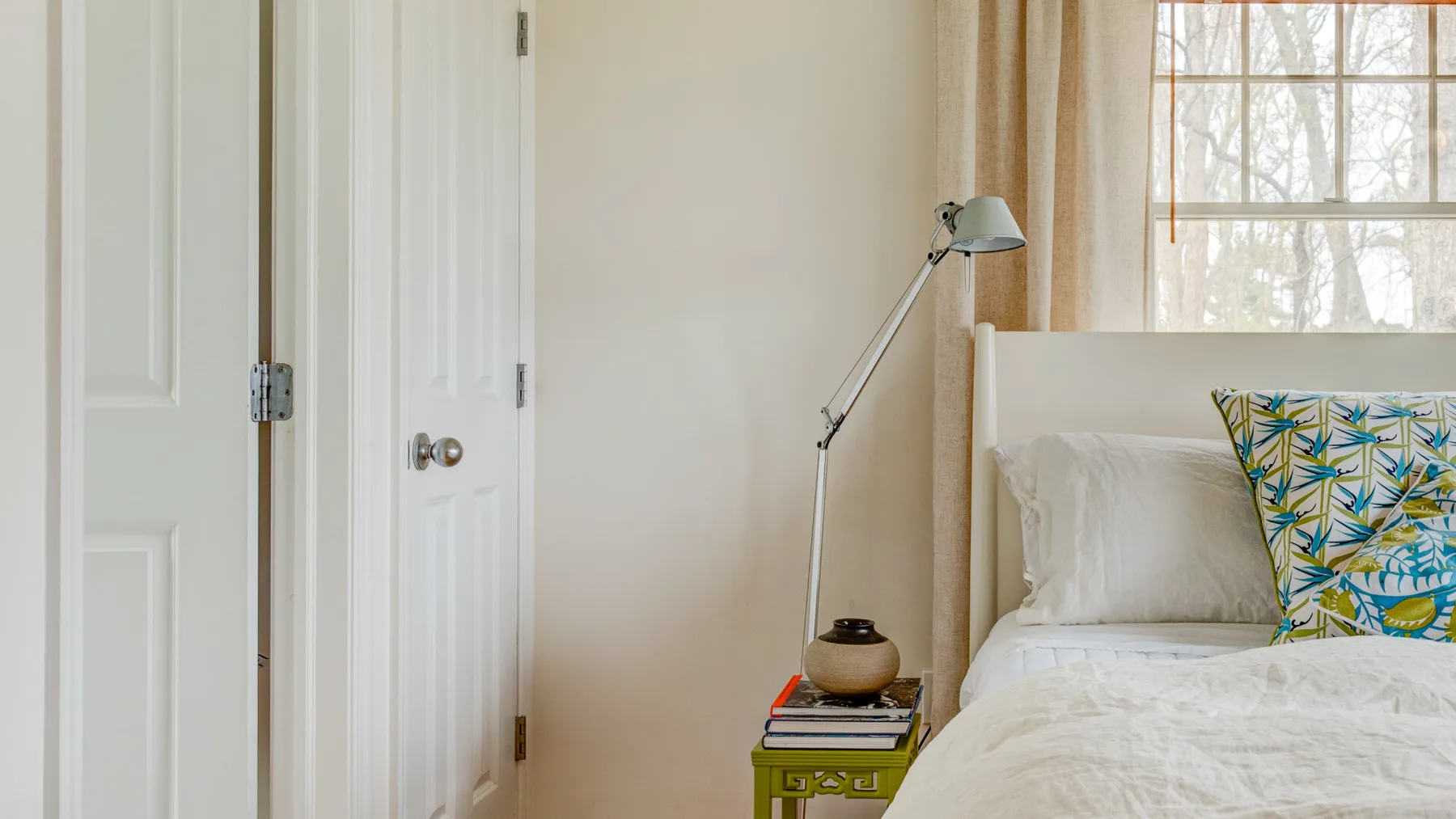 Un dormitorio luminoso con una cama junto a una ventana y una lámpara de lectura.