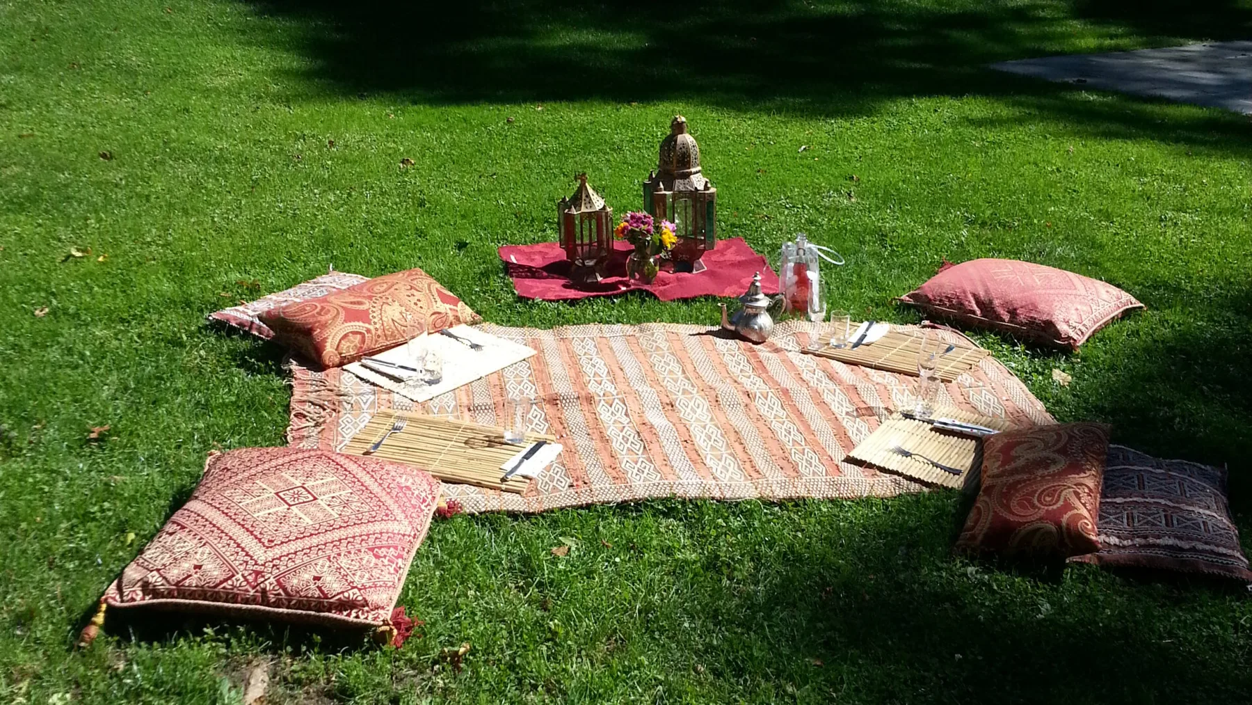 Un montaje de picnic en el césped incluye alfombras estampadas, cojines y faroles.