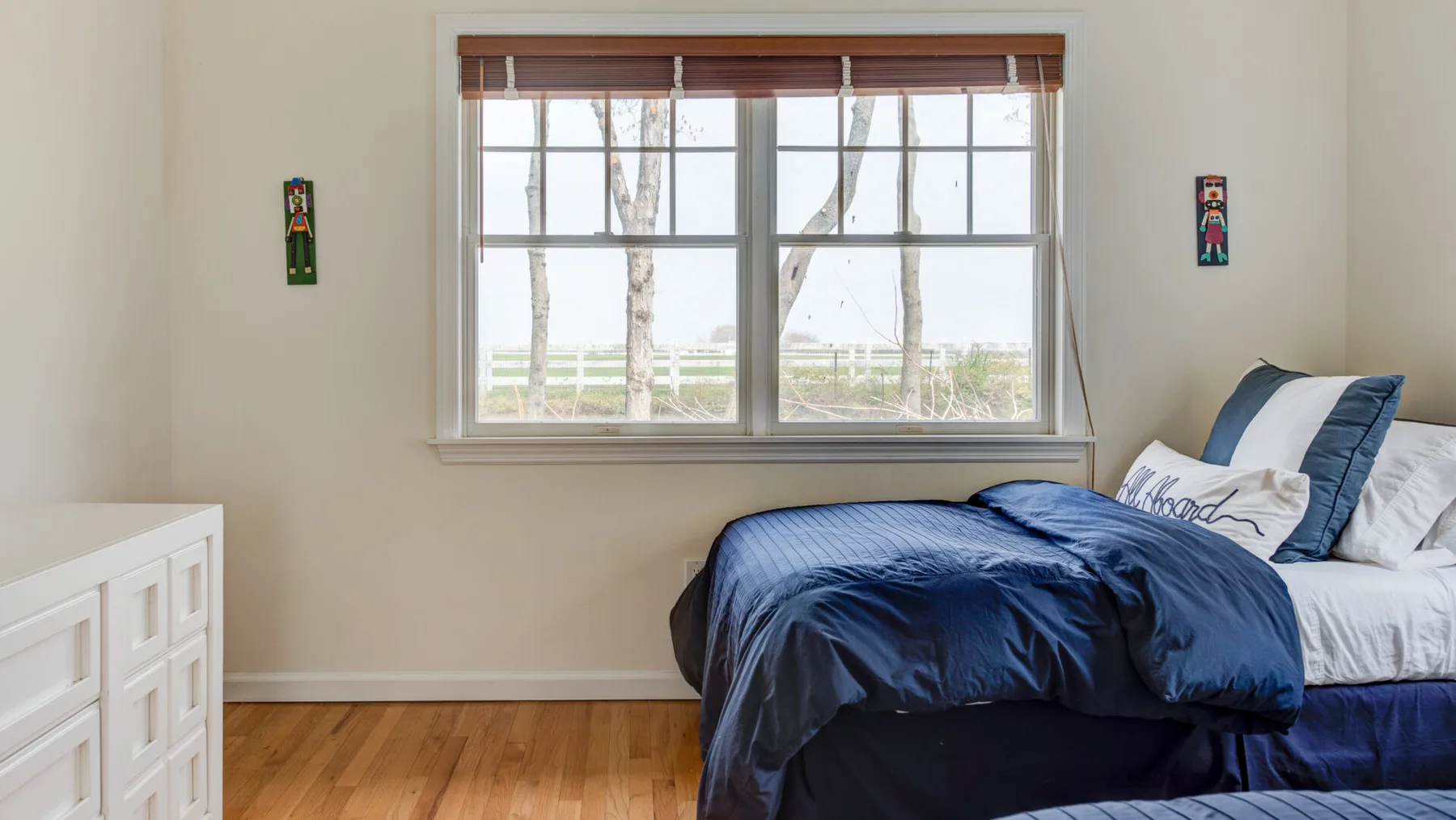 Un dormitorio con una cama bajo una ventana grande y una cómoda blanca.