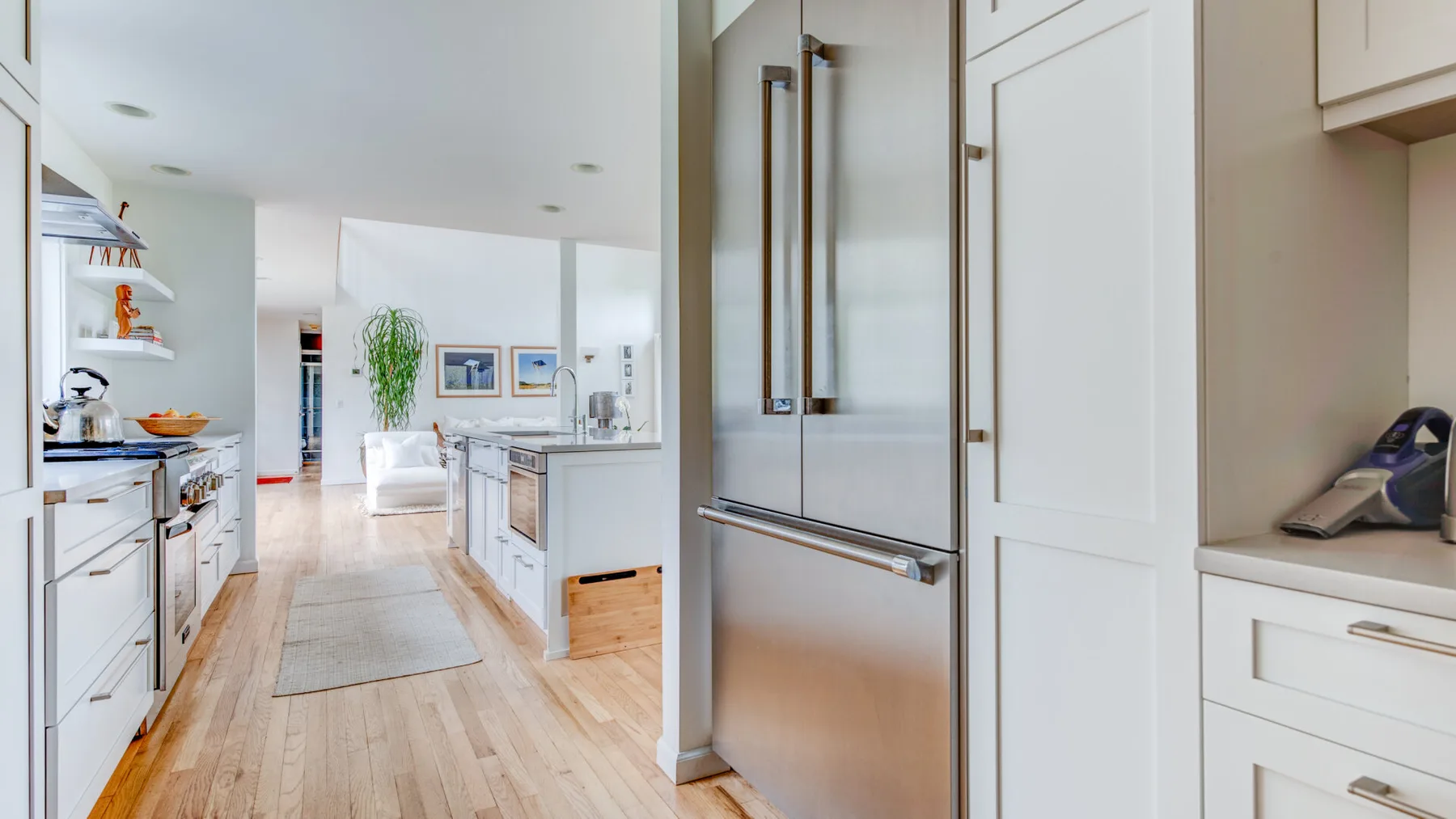 Una cocina luminosa con gabinetes blancos, un refrigerador de acero inoxidable y piso de madera clara.