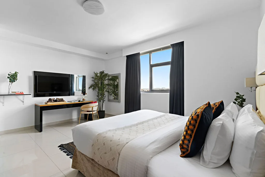 A bedroom with a bed, desk, and window with dark curtains.
