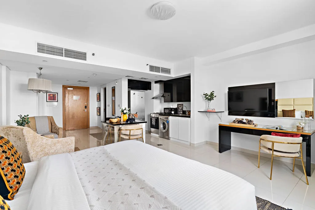 A bright open-plan room combines a bed, seating area, and compact kitchen.