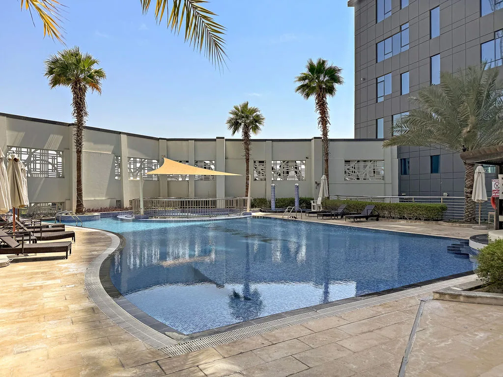 An outdoor swimming pool sits beside a modern building, with palm trees around the deck.