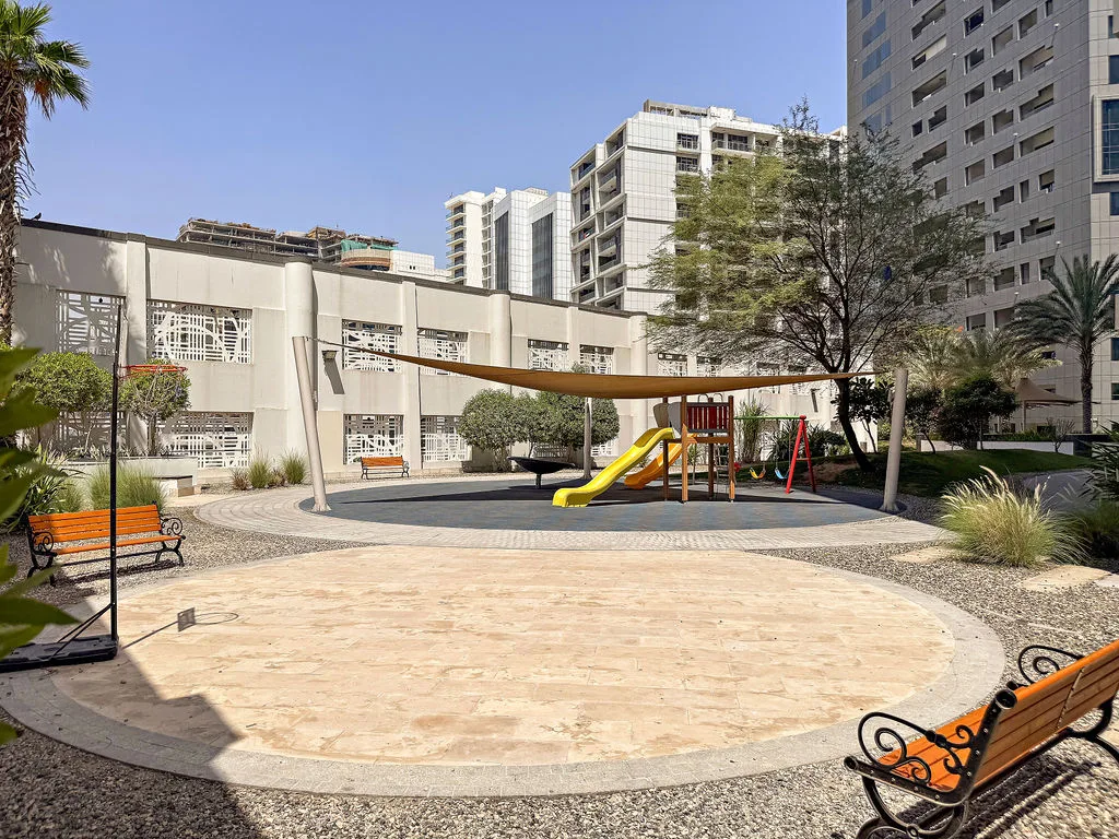 An outdoor playground with a slide and swings sits in a paved courtyard.
