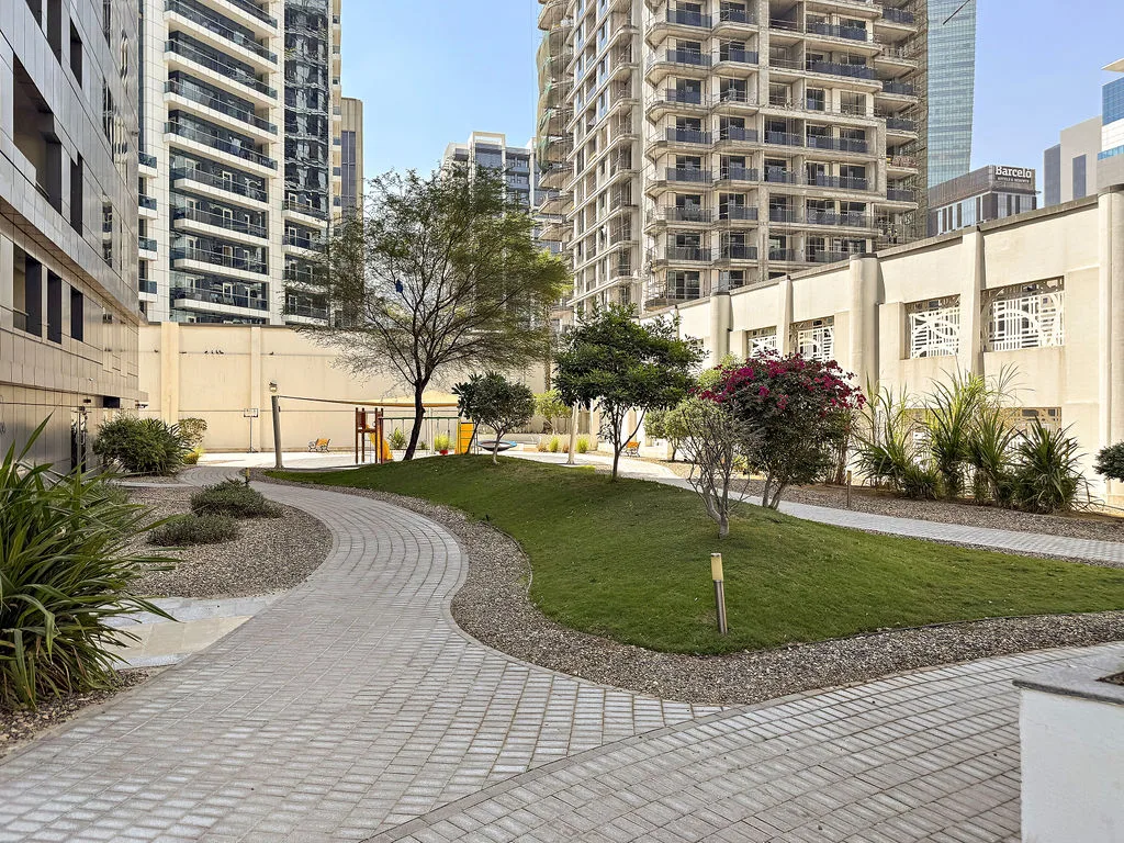 A landscaped courtyard with a curving paved path, grass, trees, and flowering shrubs.