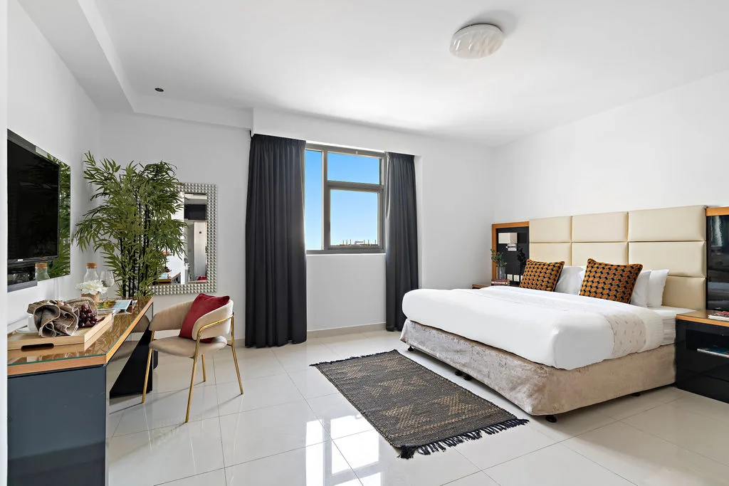 Dormitorio luminoso con una cama grande, una ventana y una zona de escritorio.