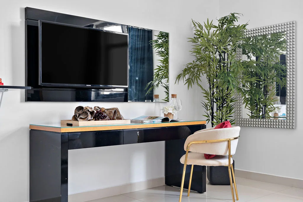 A modern desk area with a wall-mounted television, seating, and a tall leafy plant.