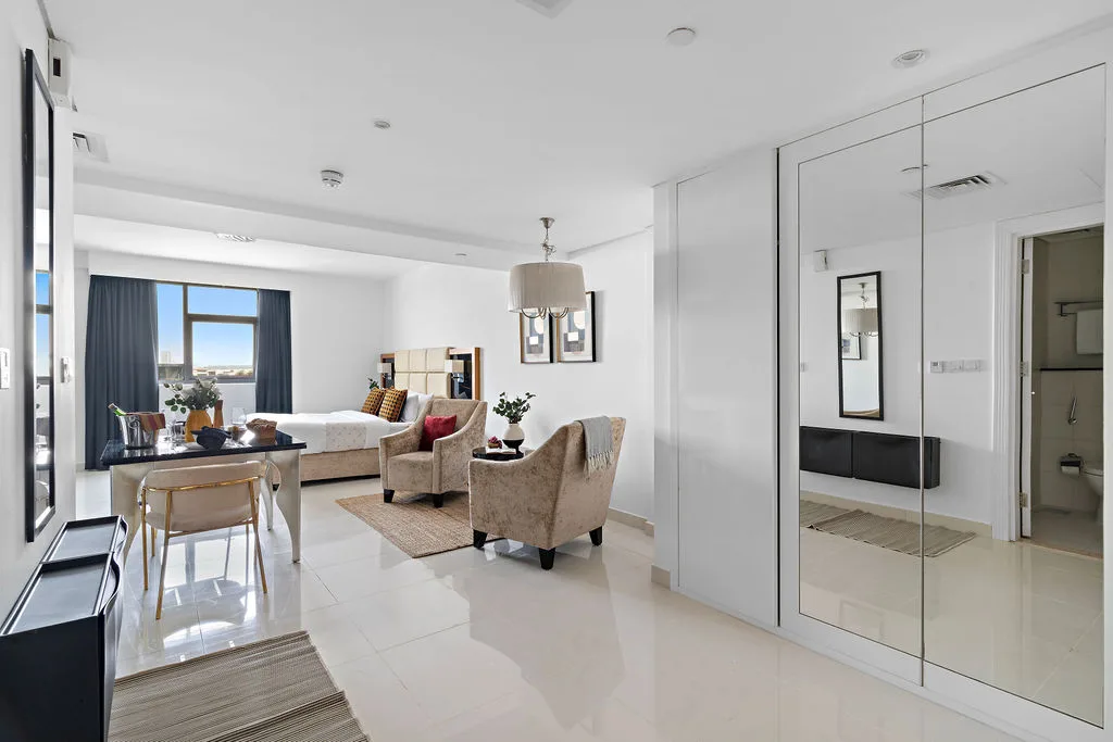 A bright living room with seating, a dining table, and a large mirrored wall.