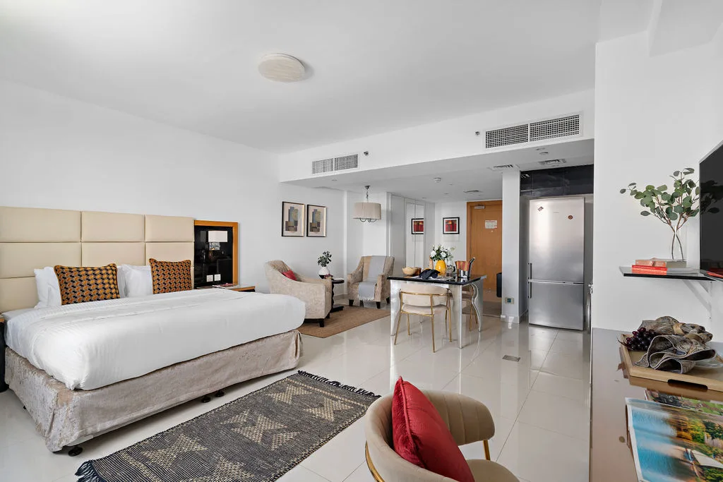 A bedroom with a bed, seating area, dining table, and kitchenette.