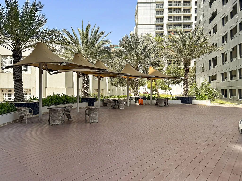An outdoor terrace has shaded seating beneath canopies, with palm trees nearby.