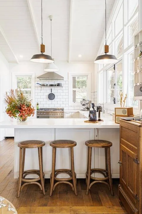 A bright kitchen with a white island and wooden bar stools.