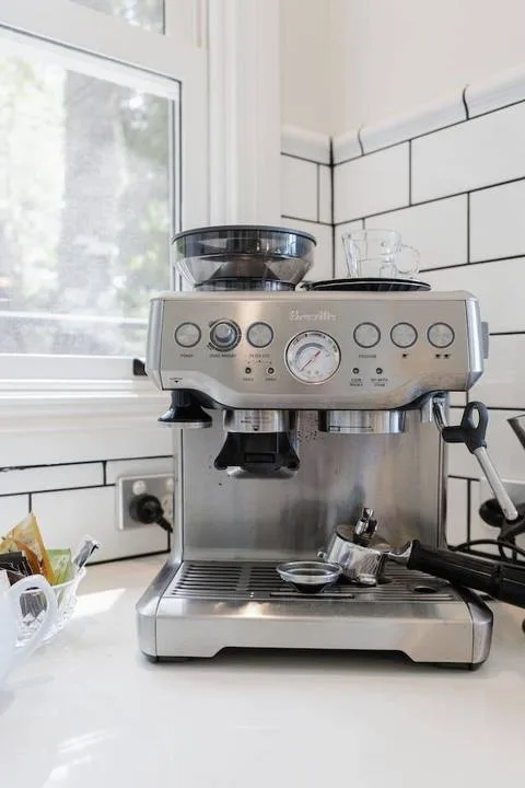 A kitchen coffee station with an espresso machine beside a window.