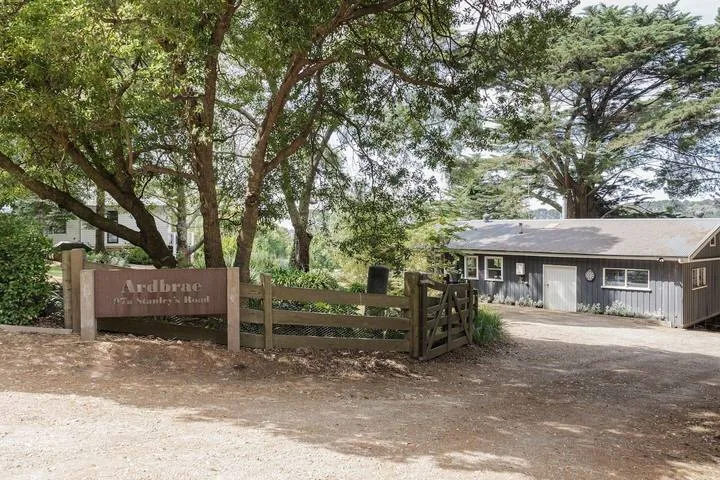 A tree-shaded entrance with a wooden gate and a low building beyond.