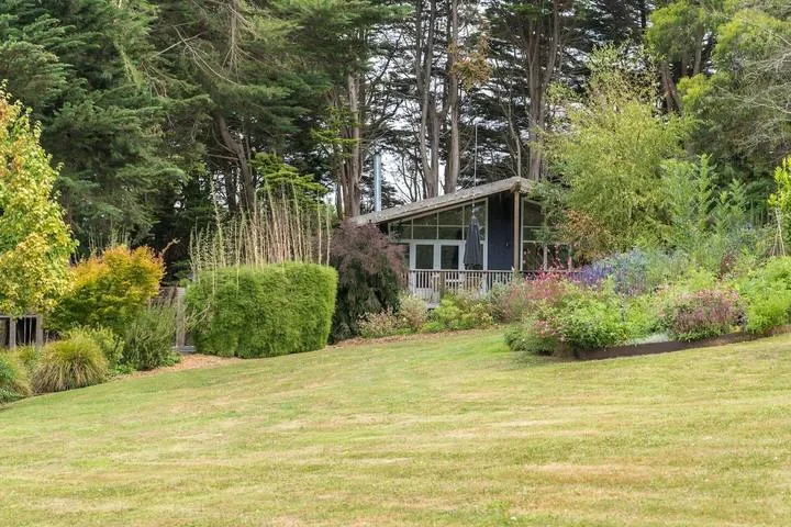 A garden lawn slopes toward a small house surrounded by trees and flowering plants.
