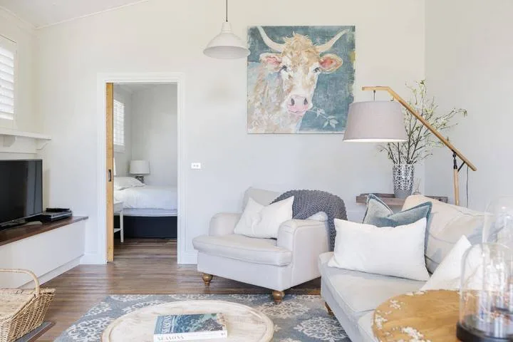 A bright living room with pale seating, a large animal portrait, and a staircase.