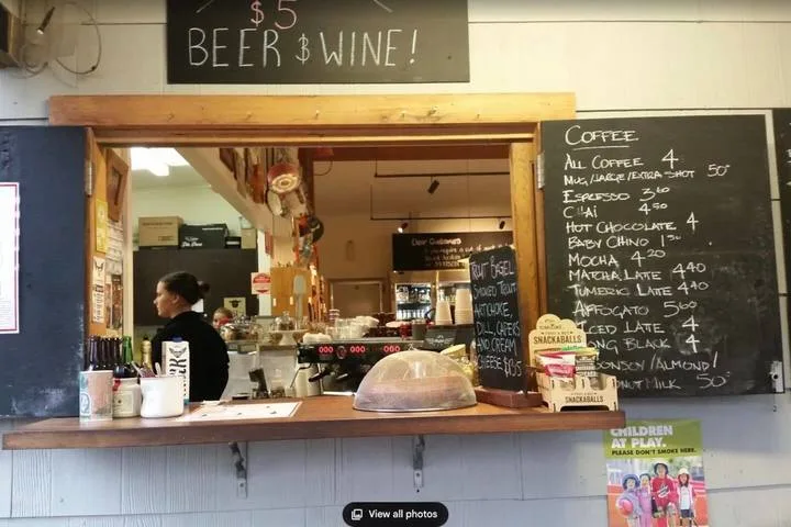 A café counter displays a coffee menu, drink supplies, and a covered pastry tray.