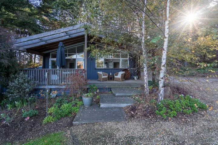 A wooded cabin entrance with a porch, outdoor seating, and a short path.