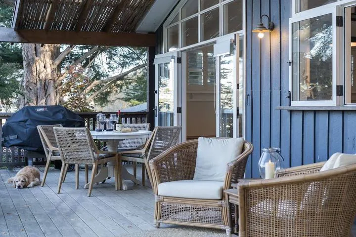 A covered outdoor deck has wicker seating and a dining table beside blue siding.