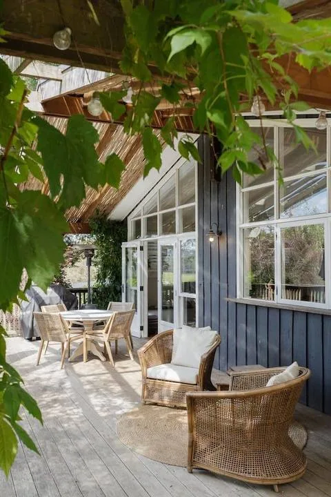 A covered outdoor patio with wicker seating and a dining table beside large windows.