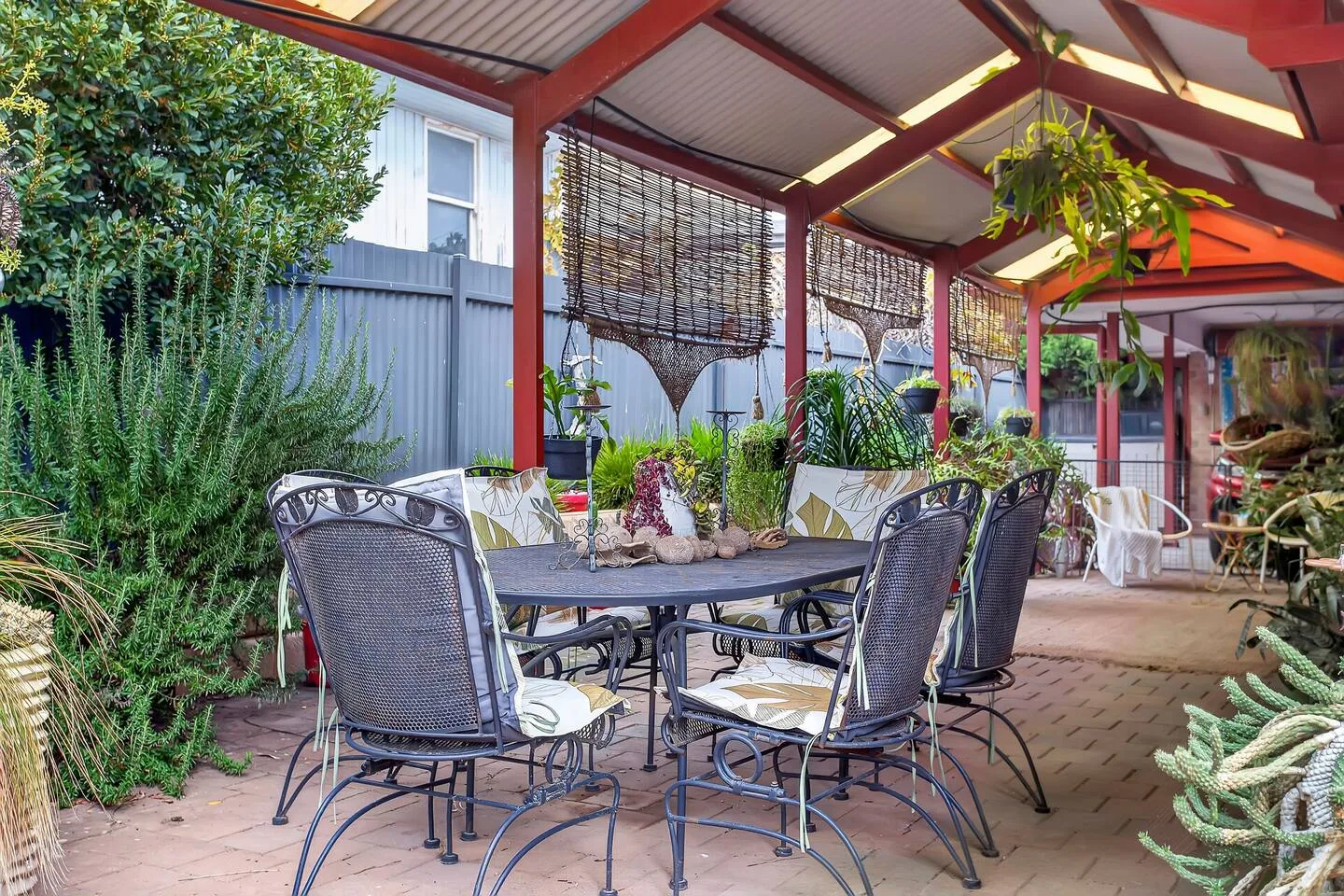 Un patio cubierto con asientos al aire libre, plantas en macetas y una mesa de comedor.